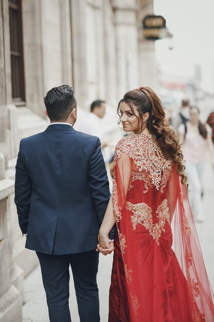 De mooie vrouw in een lange rode kleding loopt rond de stad met haar echtgenoot