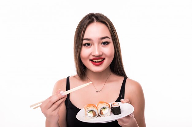 De mooie vrouw met zwart haar en rode lippen proeft suushi-broodjes die houten eetstokjes in haar hand houden
