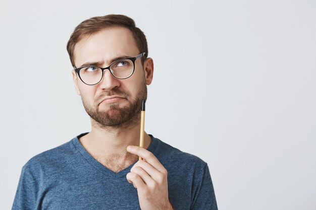 De nadenkende gebaarde mens in glazen, houdt potlood, denkend wat schrijf