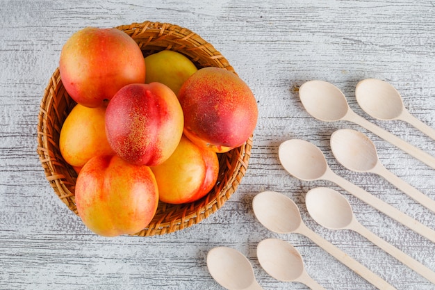 Gratis foto de nectarines in een mand met houten lepelsvlakte lagen op een grungy muur