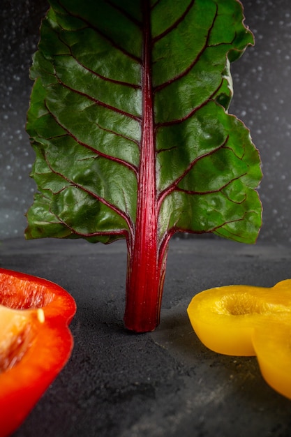 De paprika's sneden rijpe rode en gele groene paprika samen met groen blad op grijze achtergrond