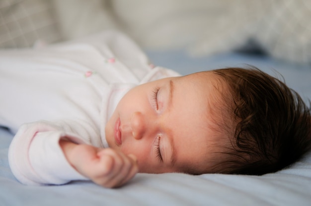 De pasgeboren slaap van het babymeisje op blauwe bladen thuis