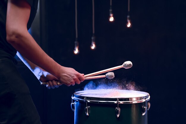 De percussionist speelt met stokken op de vloertom in een donkere kamer met mooie verlichting. Concert- en prestatieconcept.