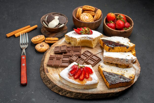 De plakjes van de vooraanzichtcake met koekjes en chocolade op donkere achtergrond