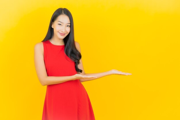De portret mooie jonge aziatische vrouw draagt rode kledingsglimlach met actie op gele muur