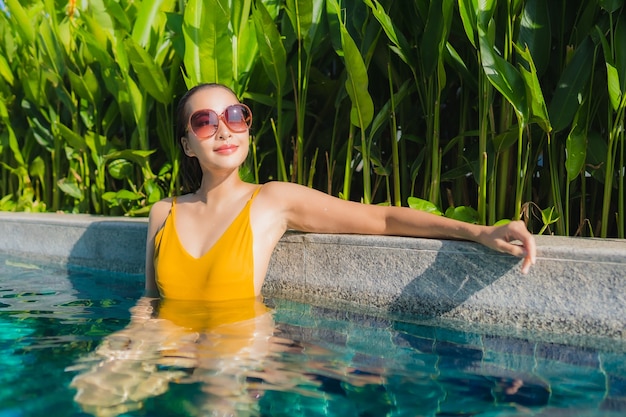 De portret mooie jonge aziatische vrouw ontspant gelukkige glimlach rond openluchtzwembad in hoteltoevlucht voor vrijetijdsvakantie