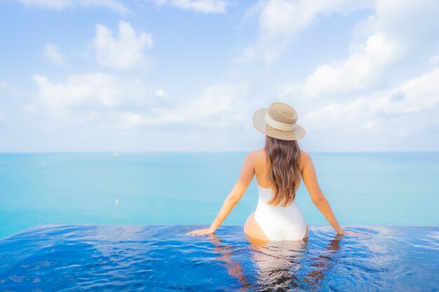 De portret mooie jonge aziatische vrouw ontspant glimlachvrije tijd rond openluchtzwembad met overzeese oceaan in reisvakantie