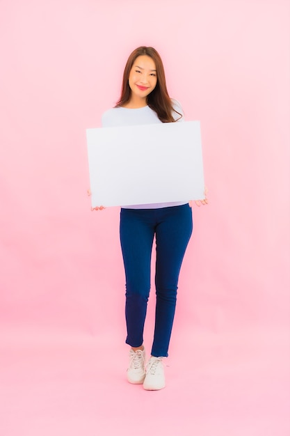 De portret mooie jonge aziatische vrouw toont leeg wit aanplakbord voor tekst op roze kleurenmuur