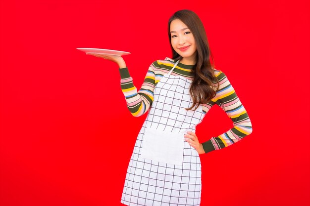 De portret mooie jonge aziatische vrouw toont lege schotel op rode muur