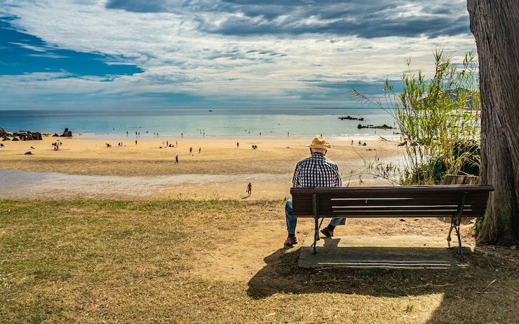Gratis Foto de rug van een oudere man die op een bankje aan de kust van de zee zit