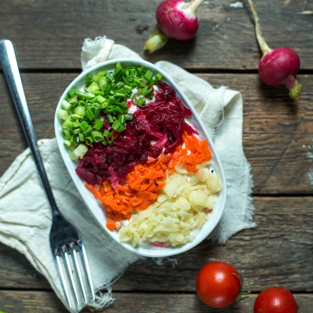 Gratis foto de saladeharing van de zijaanzicht onder een bontjas met tomaten en radijzen