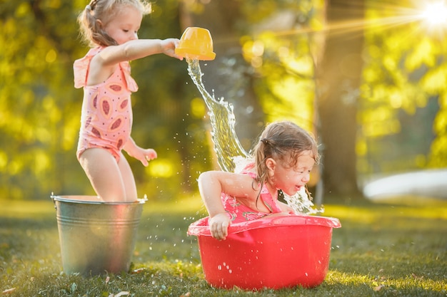 De schattige kleine blonde meisjes spelen met water spatten op het veld in de zomer