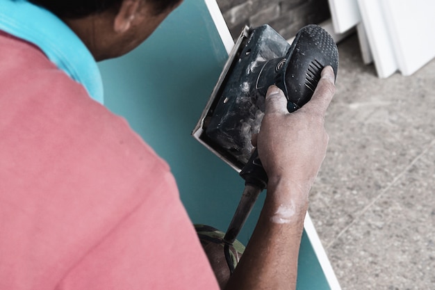 De schilder werkt aan het proces van het schilderen van meubels met behulp van een scrubmachine