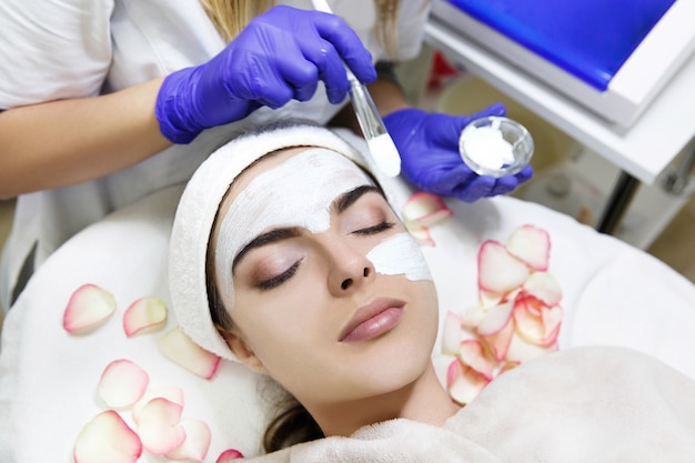 De schoonheidsspecialist past wit masker op het gezicht van de vrouw toe