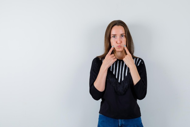 Gratis foto de serieuze vrouw legt haar wijsvingers op de wangen op een witte achtergrond