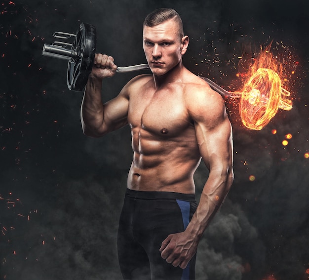 De shirtless gespierde, atletische man houdt de brandende halter op een grijze achtergrond.