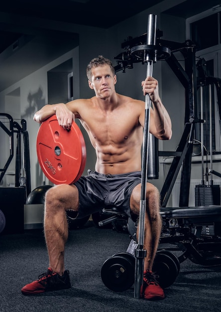 De shirtless gespierde man houdt haltergewicht in een sportschoolclub.