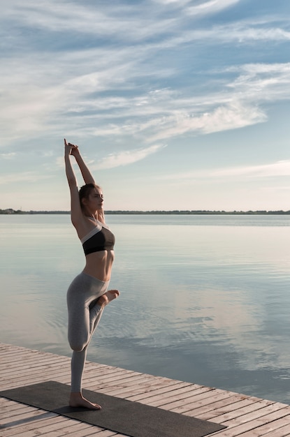 Gratis foto de sportdame die zich bij het strand bevindt maakt yogaoefeningen.