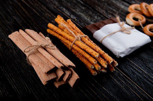 De stokken van het zijaanzichtgraan met de chocolade van broodstokken en droge ongezuurde broodjes op een zwarte houten achtergrond