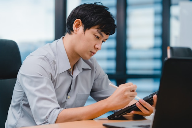 De succesvolle uitvoerende jonge zakenman slimme vrijetijdskleding die van Azië slimme pen dragen, schrijven en met digitale tabletcomputer het denken aan het werkproces van inspiratiezoekideeën in modern bureau denken.