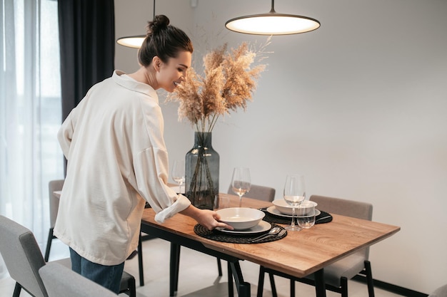 De tafel bedienen. Jonge vrouw in een wit overhemd die borden op tafel zet