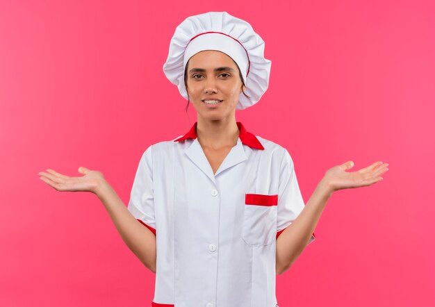 De tevreden jonge vrouwelijke kok die eenvormige chef-kok draagt spreidt handen uit