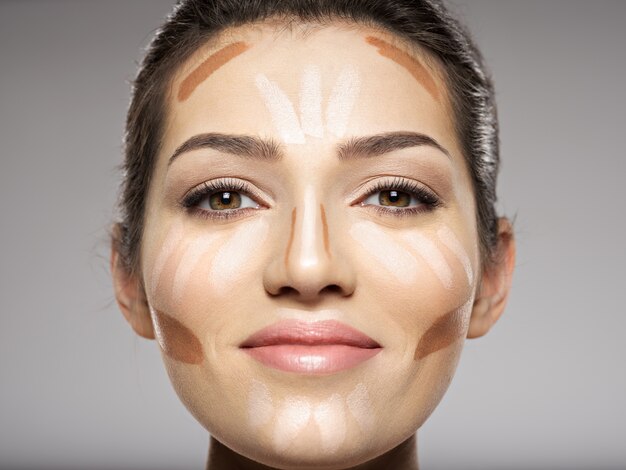 De tonale foundation van de cosmetische make-up is op het gezicht van de vrouw. Schoonheidsbehandeling concept. Meisje maakt make-up.
