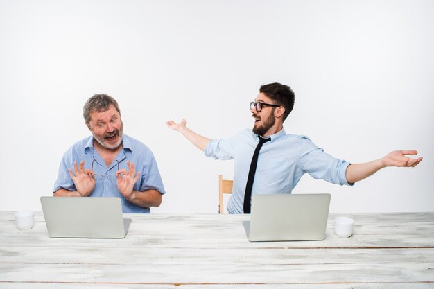 De twee collega's die op kantoor op witte achtergrond samenwerken. beiden kijken naar de computerschermen. Beiden verrast. concept van positieve emoties en goed nieuws