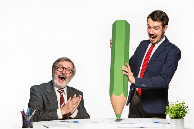 De twee collega's werken op kantoor samen met een enorm gigantisch potlood