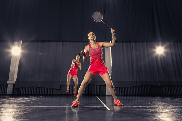 De twee jonge vrouwen die badminton spelen over gymnastiekruimte. conceptspel in een paar