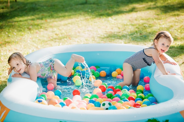 De twee kleine baby meisjes spelen met speelgoed in opblaasbaar zwembad in de zonnige zomerdag