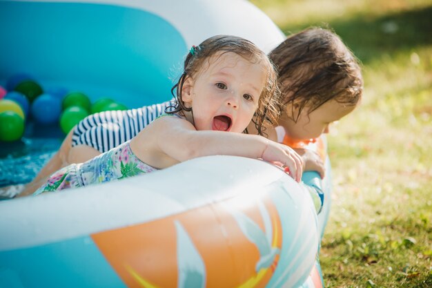 De twee kleine baby meisjes spelen met speelgoed in opblaasbaar zwembad in de zonnige zomerdag