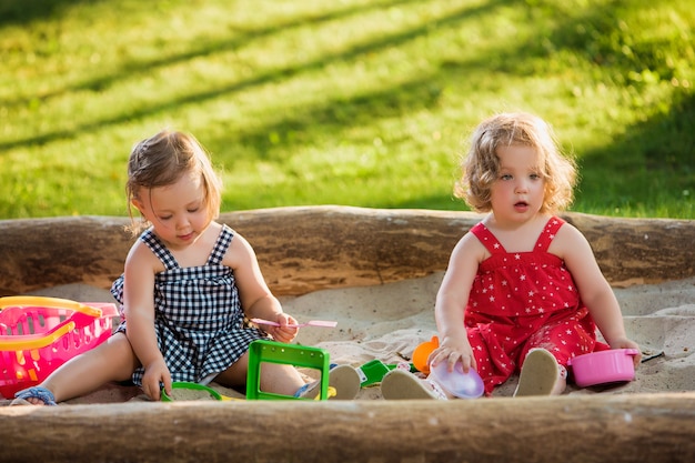 De twee kleine babymeisjes die speelgoed in zand spelen