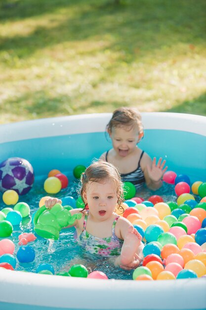 De twee twee jaar oude kleine baby meisjes spelen met speelgoed in opblaasbaar zwembad in de zonnige zomerdag