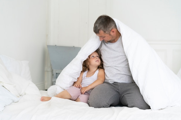 De vaderzitting van het vooraanzicht met dochter onder deken