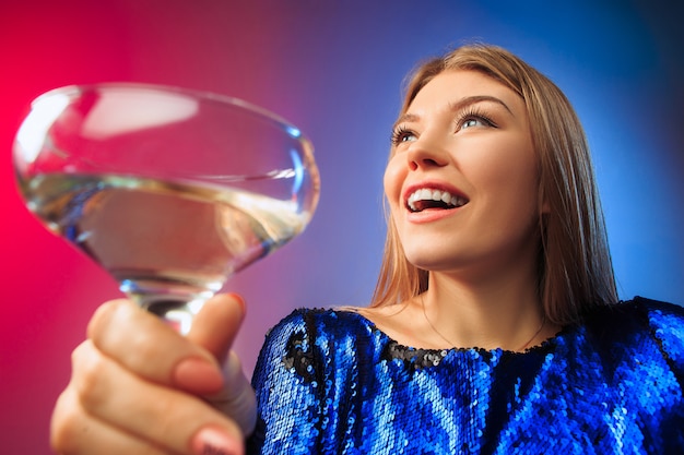 De verbaasde jonge vrouw in feestkleding poseren met glas wijn