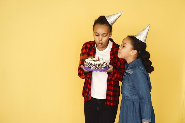 De verjaardag van kleine meisjes die op gele muur wordt geïsoleerd. Kinderen die cake houden.