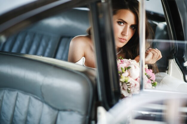 De verleidelijke bruid zit binnen een witte retro auto met leerzetels