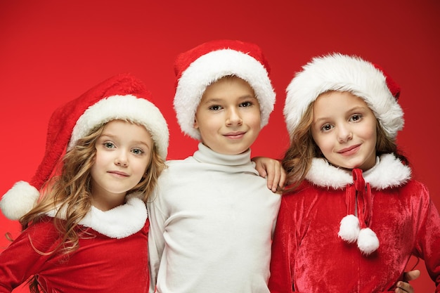 De verraste en gelukkige jongen en meisjes in santa claus hoeden met geschenkdozen in rode studio