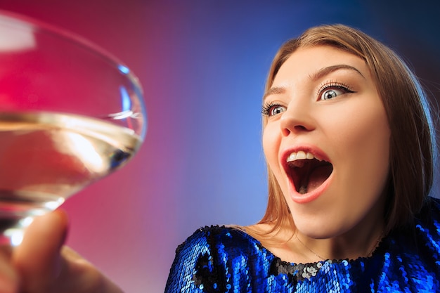 De verraste jonge vrouw in feestkleren poseren met een glas wijn.