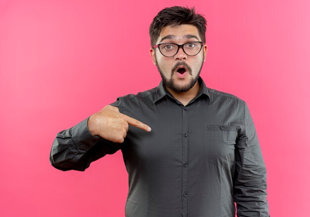 De verraste jonge zakenman die glazen draagt wijst naar zichzelf geïsoleerd op roze