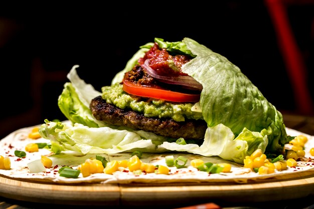 De vleeshamburger in sla verlaat guacamolesidemening van tomatenkorrels