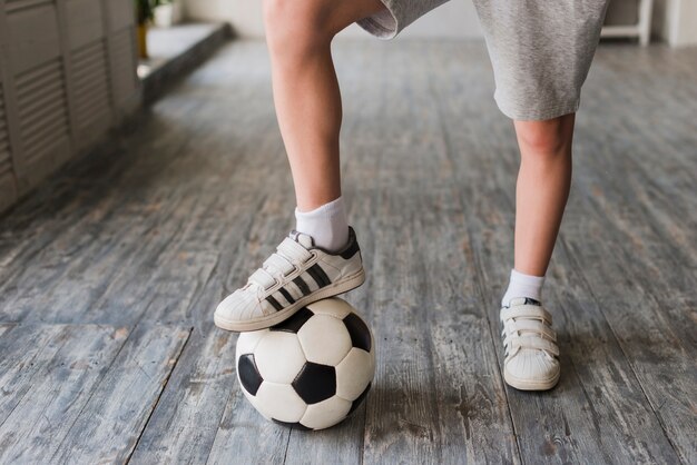 De voet van de jongen op voetbalbal over de hardhoutvloer