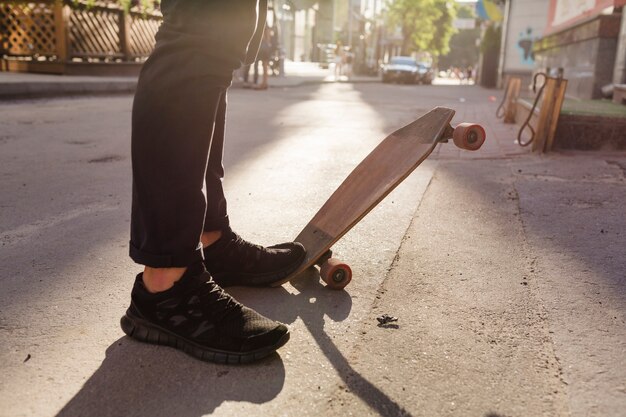 De voeten van de persoon en houten skateboard op straat