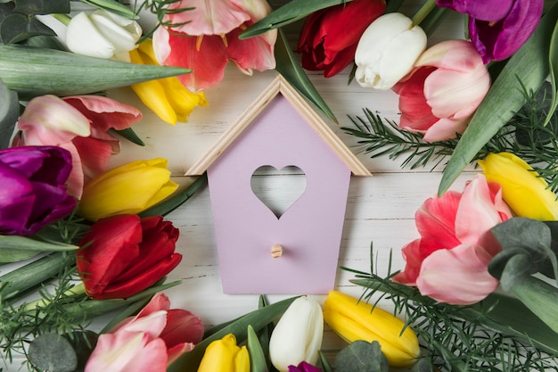 De vogelhuis van de hartvorm met kleurrijke tulpen op houten bureau wordt omringd dat