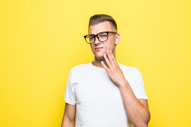 De vrij jonge jongen raakt zijn gezicht aan gekleed in wit t-shirt en transparante glazen die op geel worden geïsoleerd