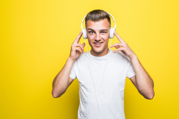 De vrij knappe mens in wit t-shirt luistert muziek met zijn nieuwe oortelefoons die op gele muur wordt geïsoleerd