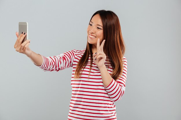 De vrolijke jonge Aziatische vrouw maakt selfie telefonisch