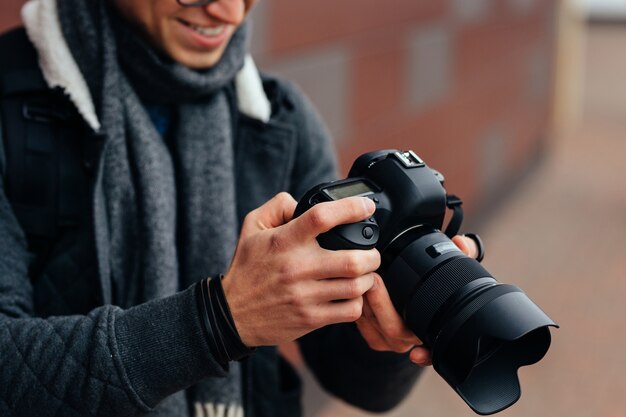 De vrolijke jonge man bekijkt foto&#39;s in de camera. Gekleed modieus jasje, grijze sjaal