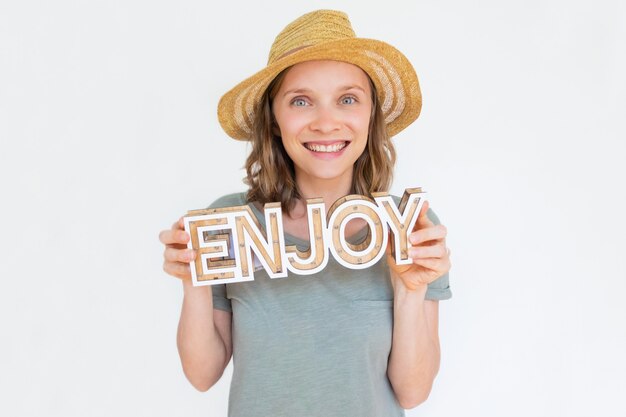 De vrolijke jonge vrouw in de hoedenholding van het de zomerstro geniet van woord